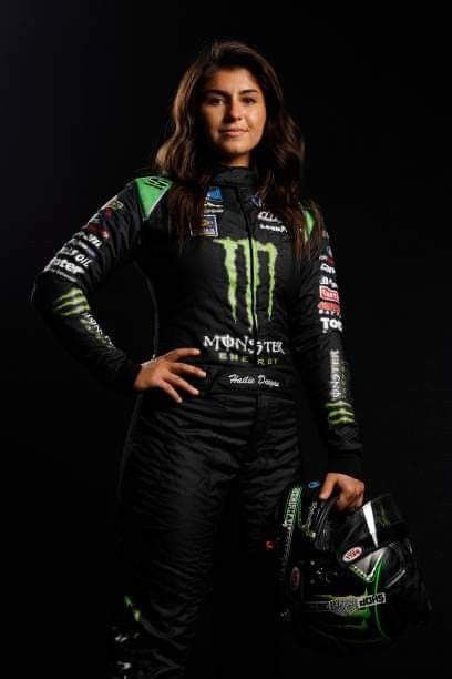 A Woman In A Racing Suit Is Posing For A Photo With Her Helmet And Glove