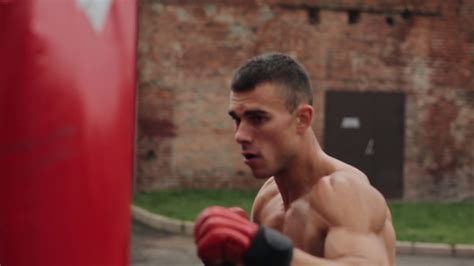 Shirtless muscular boxer punching a punching bag while 