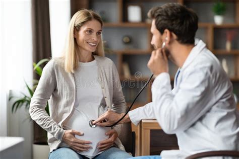 Male Gynecologist With Stethoscope Examining Belly Of Pregnant Female Patient Stock Image