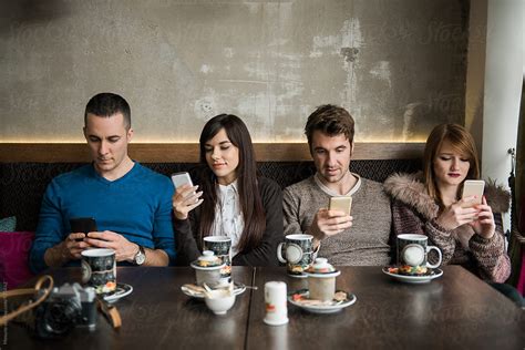 Four Friends Looking At Their Mobile Phone In A Cafe Del Colaborador