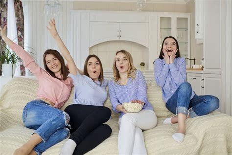 Chicas Jóvenes Que Ven La Tv Comiendo Las Palomitas Que Se Sientan En El Sofá Imagen De Archivo