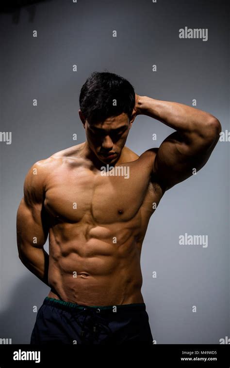 A Muscular Asian Fitness Model Flexes His Muscular Abdomen With An Arm