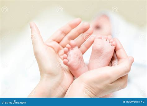 Mother Holding Feet Of Newborn Baby Infant Legs In Parent Hand Child