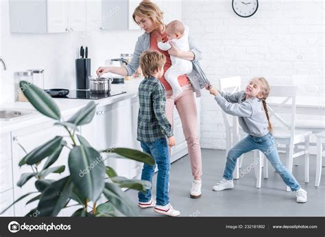 Tired Mother Holding Infant Child Cooking While Naughty Children