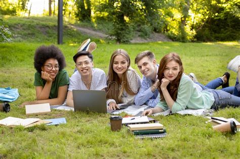 Group Of International College Students Lying On Lawn In Park Studying