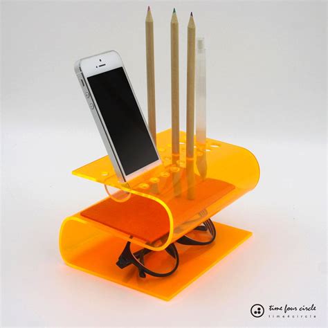 A Cell Phone And Some Pencils In A Holder With An Orange Stand On It