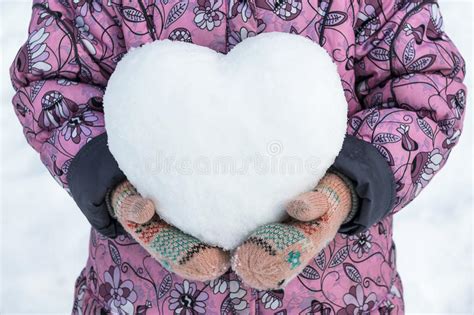 Girl In Coat And Mittens Holding A Snowball In The Shape Of A Heart