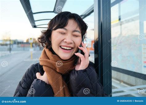 Close Up Of Asian Girl On Bus Stop Laughs Over Phone Conversation Talks On Telephone While