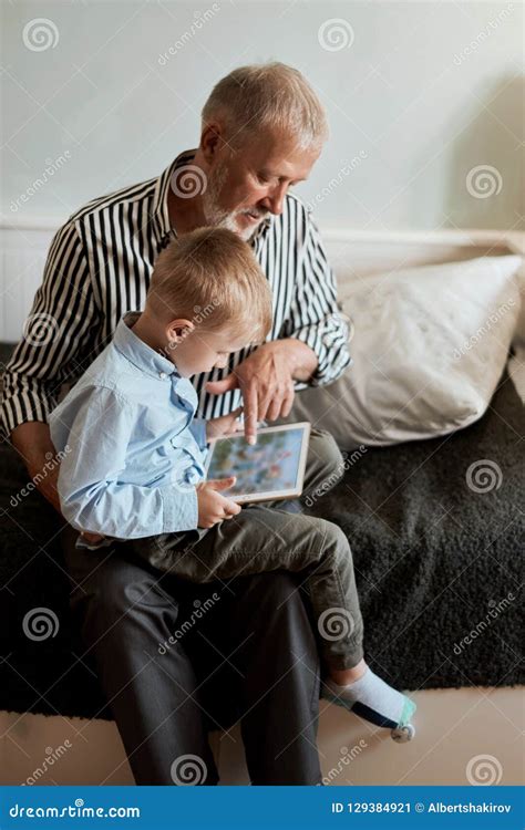 Grandfather And Grandson Using Digital Tablet While Sitting On Couch