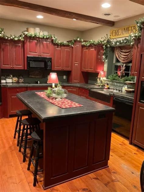 A Kitchen Decorated For Christmas With Red Cabinets And Black Counter