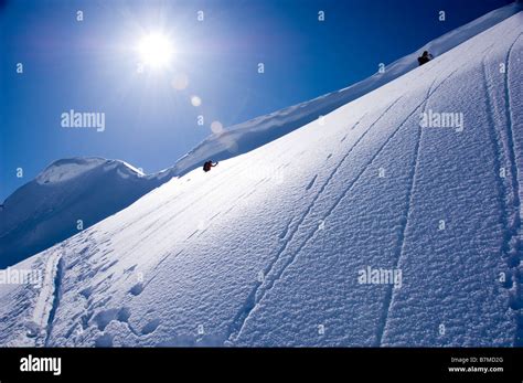 Ski Alpinists Ascending A Steep Slope Under A Cornice In The Swiss Alps