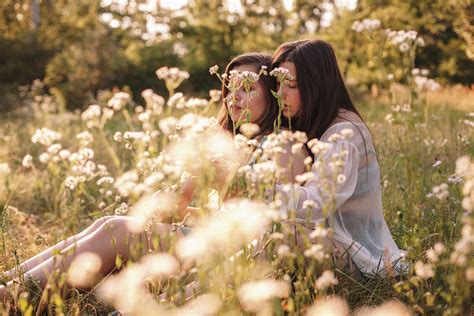 Lesbian Couple Talking Sitting Amidst Flowers On Summer Field