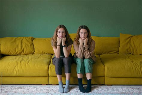 Two Girls Of Norwegian Appearance Sit Symmetrically On A Yellow Sofa By Stocksy Contributor