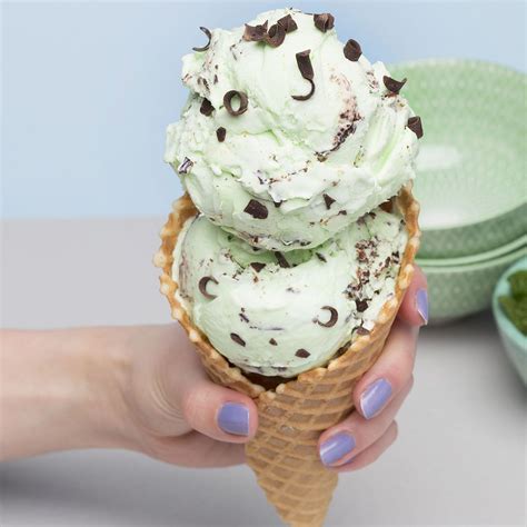 Left hand holding waffle cone with double scoops of mint chocolate chip ice cream on a light 