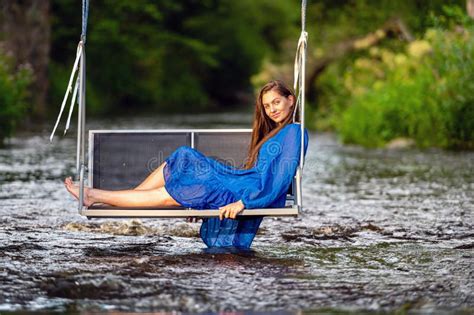 A Joyful Young Woman Swings On A Rope Swing Across A Fast Flowing River