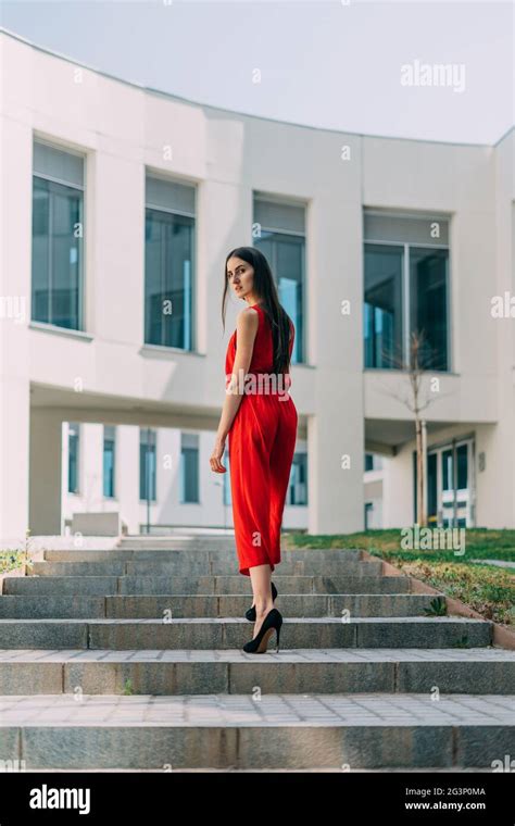 Young Business Woman In Red Dress Walking Up Stairs And Looking At