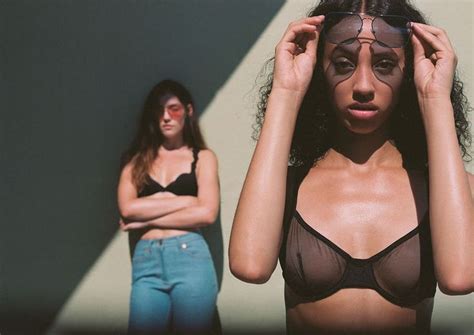 Two Women Standing Next To Each Other With Their Arms On Their Head And One Wearing A Bra