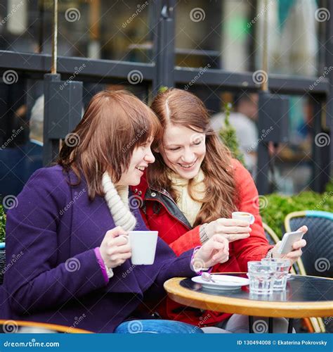 Two Girls In Cafe Drinking Coffee And Using Mobile Phone In Paris