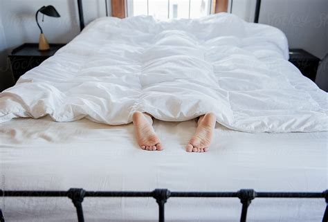 feet stick out of white bed covers by stocksy contributor cara dolan stocksy