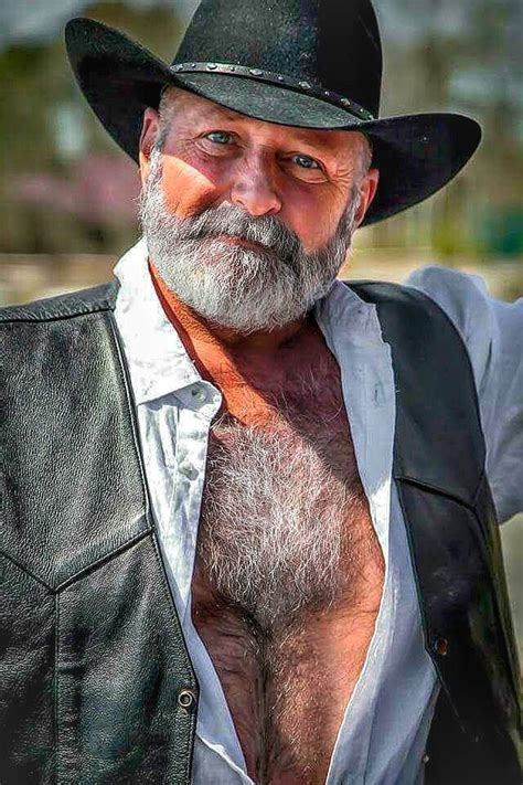 A Man With A Beard Wearing A Black Hat And Leather Jacket Posing For The Camera