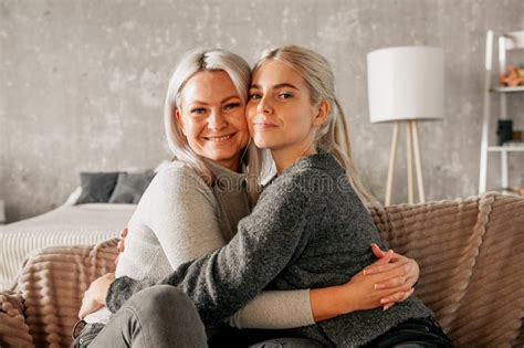 Mother And Daughter Of A Blonde Cuddle At Home On The Couch Show Love And Understanding Stock