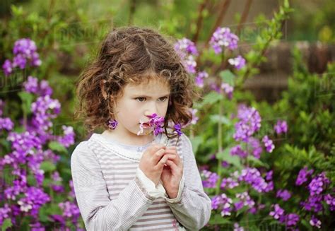 A Little Girl Smelling Flowers In A Garden Stock Photo Dissolve
