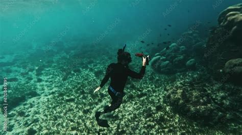Diver In Wetsuit Underwater Capturing Media Of Marine Life And Ascends