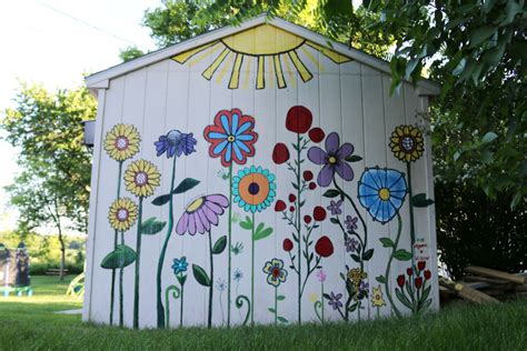 A Painted Outhouse In The Grass With Flowers And Sunbursts On It