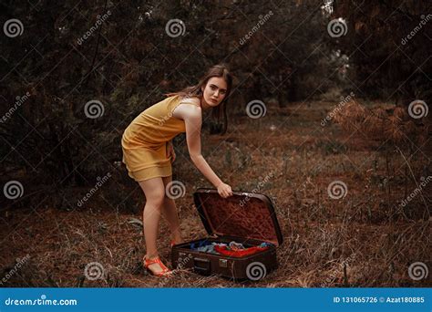 Young Beautiful Girl Takes Off A Yellow Dress To Dress Clothes From A Vintage Suitcase Stock