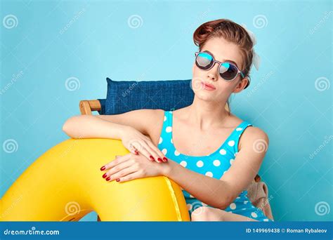 Blonde In A Bathing Suit And Glasses Sitting On A Deck Chair With An Inflatable Circle Stock