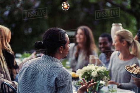 Rear View Of Man Sitting At Dining Table With Friends At Outdoor Dinner