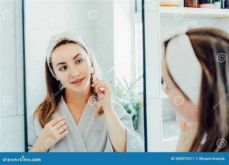 Young Woman In Bathrobe Looking In Mirror And Making Face Massage With Jade Roller In The