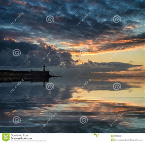 Beautiful Vibrant Sunrise Sky Over Calm Water Ocean With Lighthouse And