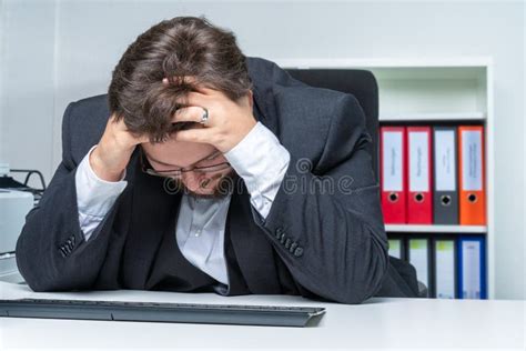 An Over Worked Businessman In The Office Holds His Head Stock Photo