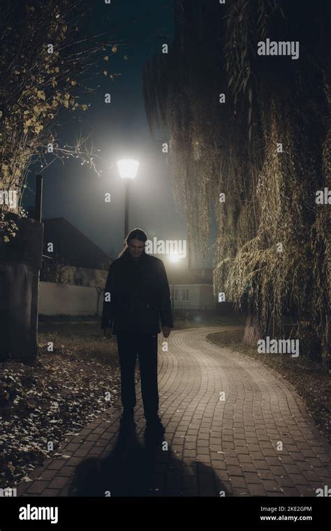 Sad Man Alone Walking Along The Alley In Night Foggy Park Stock Photo