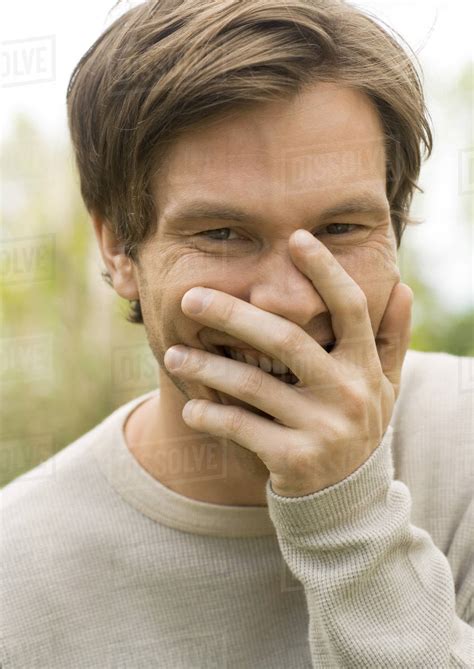 Young Man Laughing And Covering Mouth With Hand Portrait Stock Photo