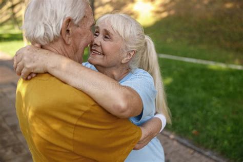 Smiling Mature Woman With Husband In Sportswear Hug In Green Park Stock