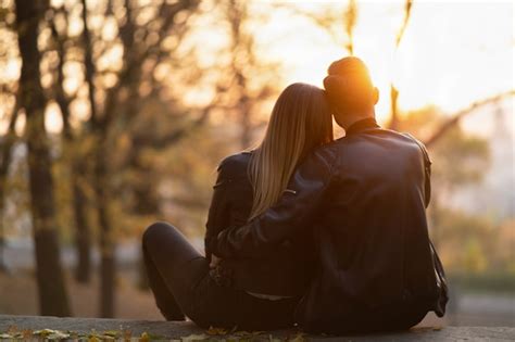Premium Photo A Romantic Couple Sitting On A Bench Hugging And Watching The Sunset In The Park
