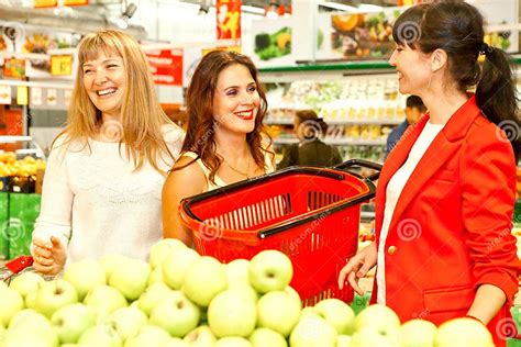Three Beautiful Girls Have Fun Laughing In A Grocery Store With A Red Basket In Their Hands