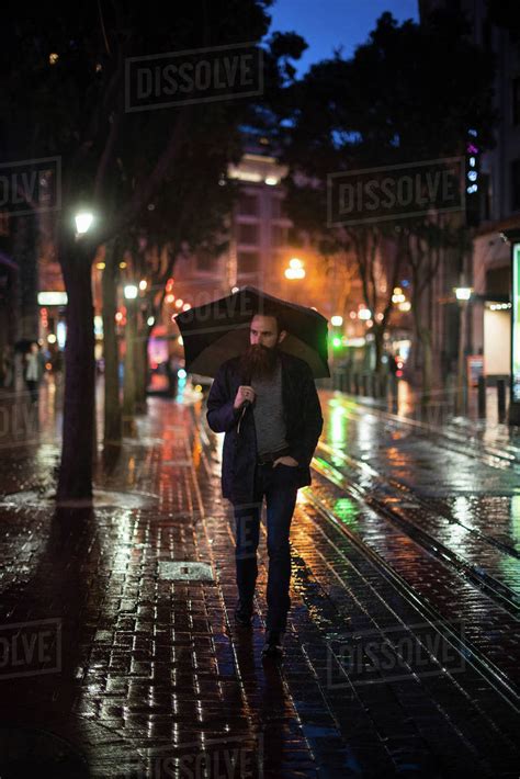 Mid Adult Man Walking In City At Night Using Umbrella Downtown San