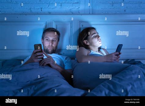 Couple Affected By Technology Addiction Ignoring At Each Other In Apathy And Anger Lying In Bed