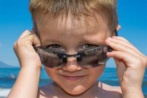 A Beautiful Little Boy Posing On A Beach By The Sea With Sunglasses