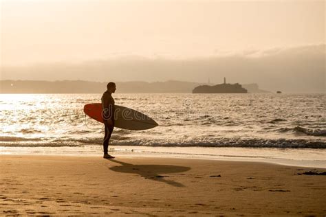 Rear View Of Strong Surfer With Surfboard On The Beach At Sunset Or