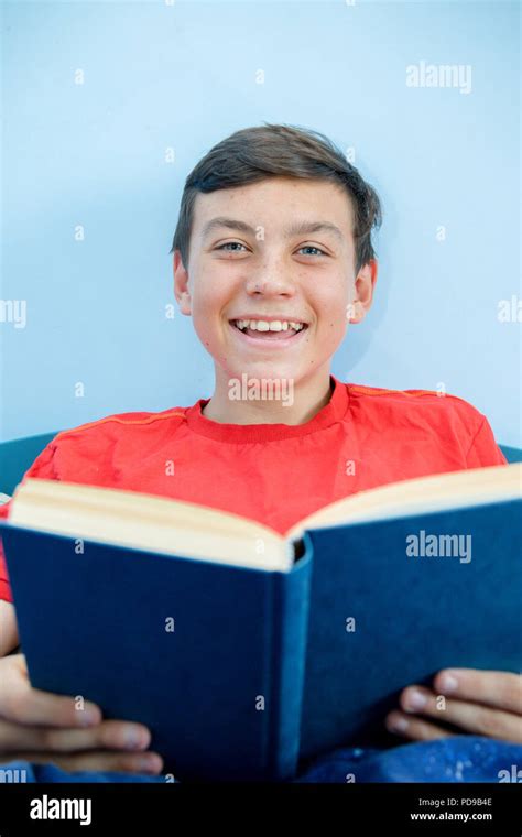 Caucasian Teenage Boy Reading A Book Laying On A Bed Laughing Stock