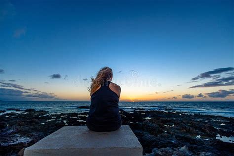 Back View Of A Female Sitting On A Shore And Looking At Calm Sea During