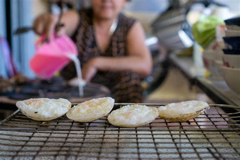 vietnamese banh can rice cakes on a barbecue grill grid with vietnamese woman preparing food in