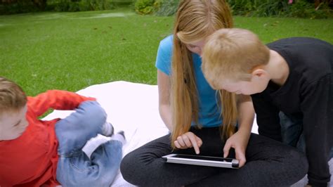 An Older Sister Shows Her Two Younger Brothers Something On A Tablet