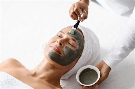 Cosmetology Beautician At Spa Salon Applying Clay Mask To Middle Aged