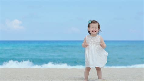 Smiley Cute Girl Baby Is Standing On Beach Sand Wearing