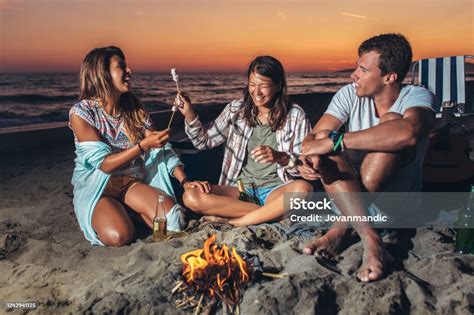 Grupa Przyjaciół Relaksująca Się Przy Ognisku Na Plaży O Zachodzie Słońca Zdjęcia Stockowe I